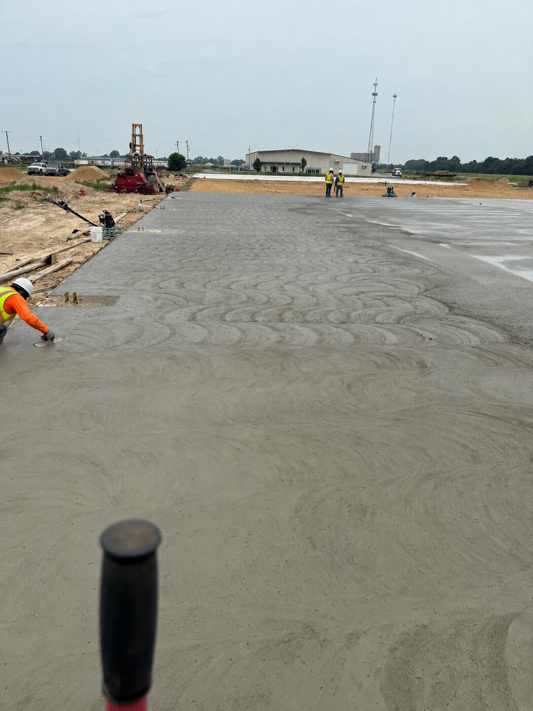 Freshly laser-screeded industrial concrete slab with crew finishing the surface at a warehouse site